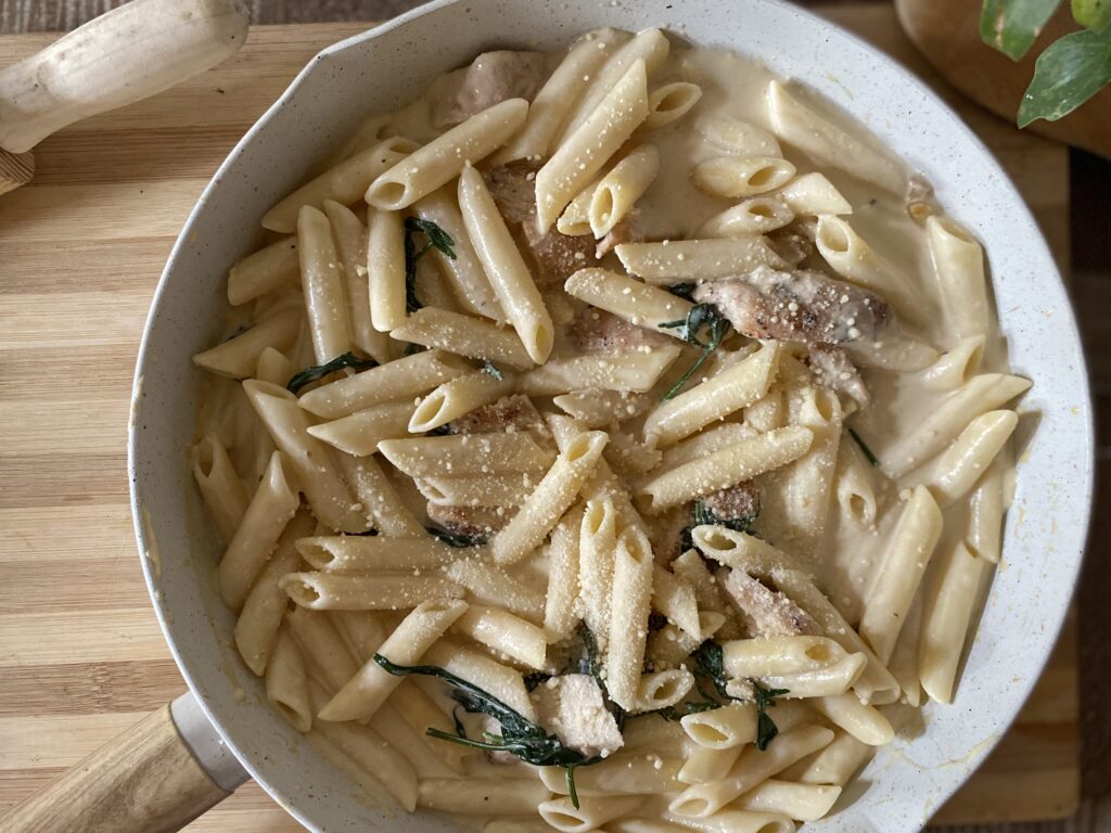 Creamy Chicken Penne: A close-up of penne pasta in a rich, creamy sauce with cooked chicken pieces, garnished with fresh herbs and grated cheese, served in a white pan.