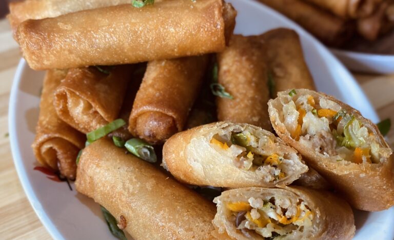 Many spring roll and there are 3 half cut, placed on an oval shape plate.