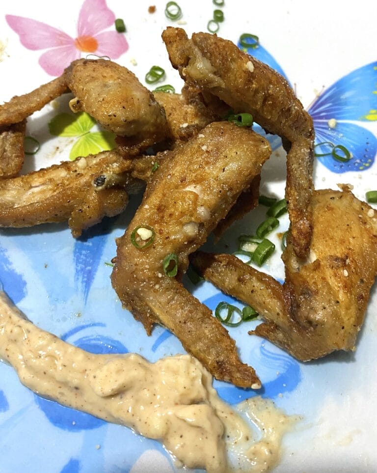 Five pieces of fried chicken wings with Parmesan sauce are placed on a plate with a bluish flowery design.