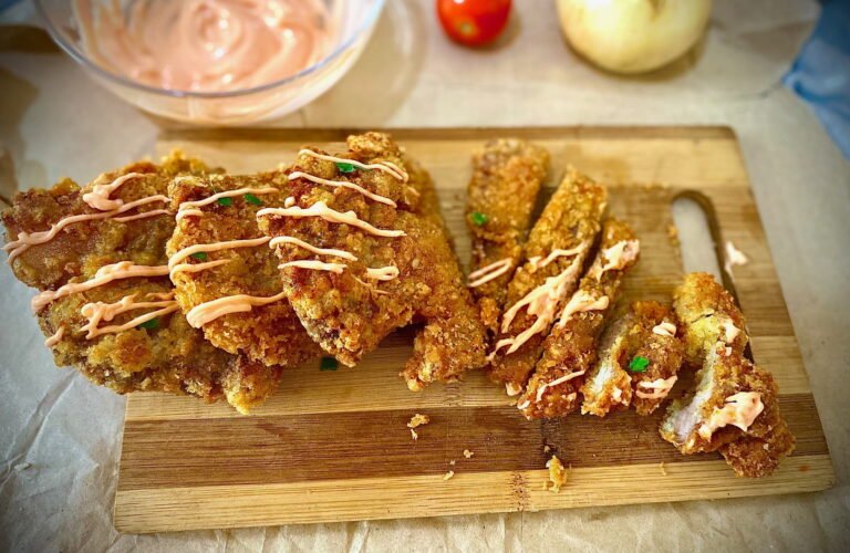 Four perfectly cooked pieces of breaded pork, one chopped into a rectangular shape, are placed on a wooden chopping board.