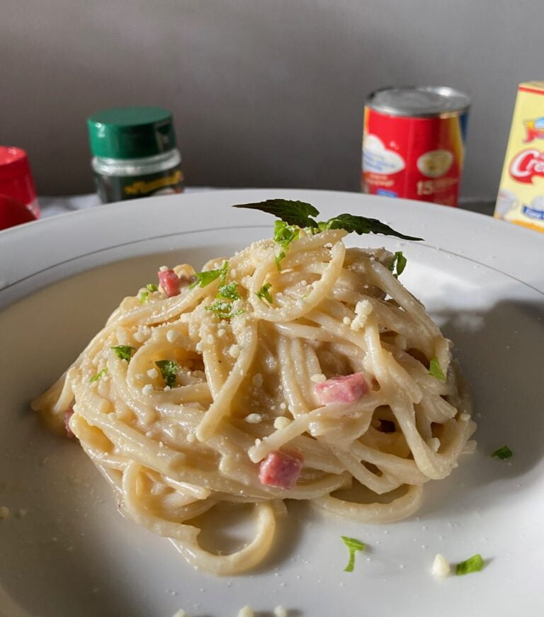 Carbonara nicely placed on a ceramic plate, garnished with shredded cheese and celery on top. Side way view.