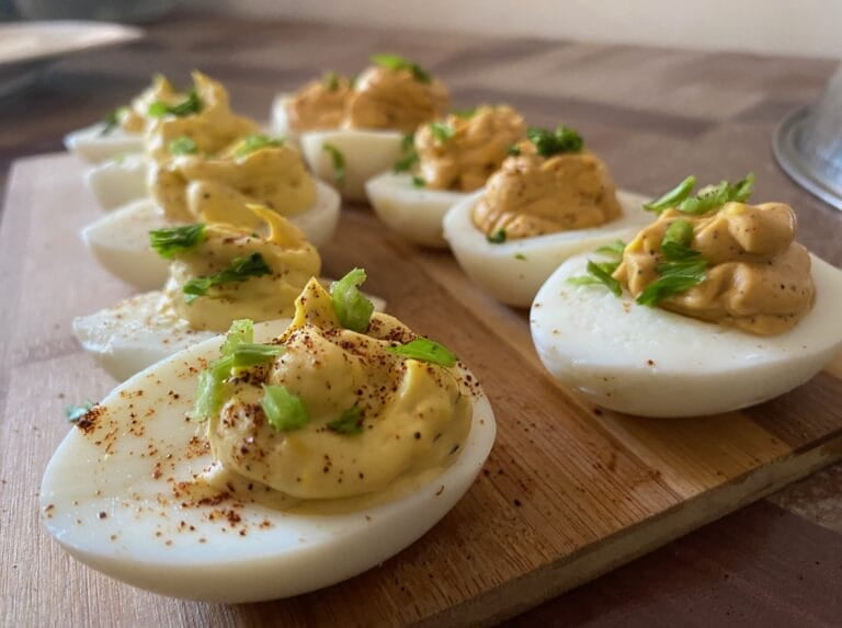 Deviled eggs garnished with celery and chili powder placed on a chopping board. 