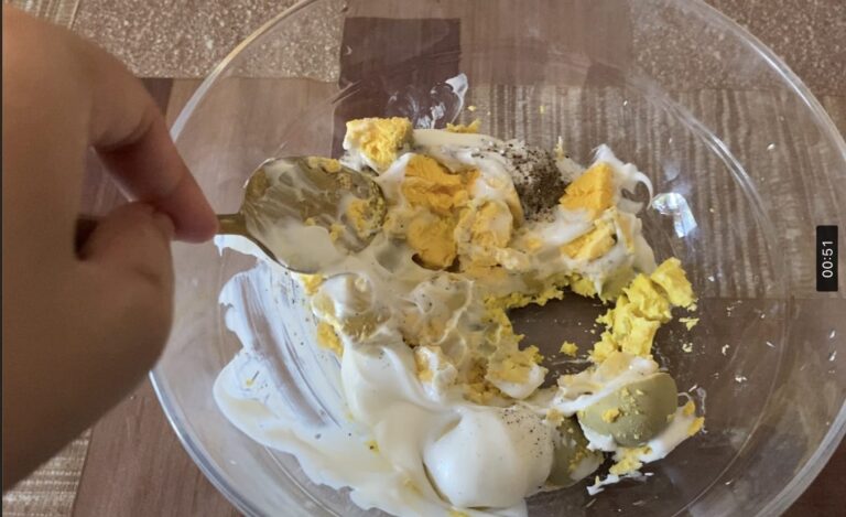 Eggs yolk, mayonnaise, and seasoning are being mixed together using a gold spoon.