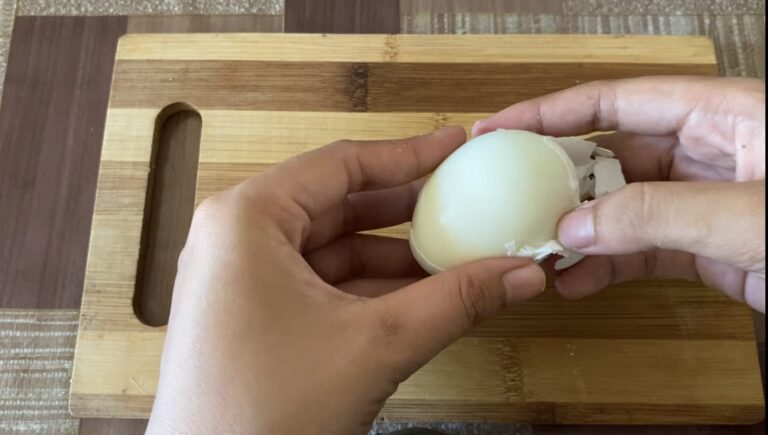 Two hands peeling off the shell of an egg.