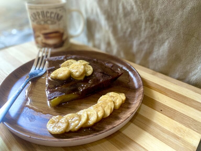 A slice of banana cake in a plate, topped with slices of banana and honey.